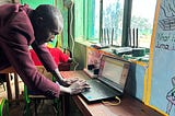 A teacher stands up using Kolibri on a laptop on the desk in front of him.