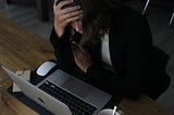 Woman leaning over laptop with her head in her hand, looking sad and tired.