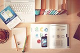 An work desk filled with a laptop, books, magazine, and a iphone.