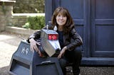 Elisabeth Sladen as Sarah Jane Smith, posing with K9 in front of the TARDIS.