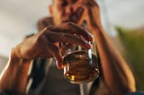 Man holding a glass of alcohol with one hand to his face