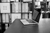 Laptop on a table. In the background shelfs.