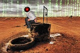 A lonely mud-brick well in a brown desert. It has been modified to add a ‘caganar’ — a traditional Spanish figure of a man crouching down and defecating — perched on the edge of the well. The caganar’s head has been replaced with the menacing red eye of HAL9000 from Kubrick’s ‘2001: A Space Odyssey.’ The sky behind this scene has been blended with a ‘code waterfall’ effect as seen in the credit sequences of the Wachowskis’ ‘Matrix’ movies. Image: Cryteria (modified) https://commons.wikimedia.or