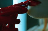 close up of woman painting lips red with bloody red hand