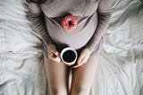 A pregnant woman holding a coffee cup and a doughnut