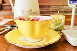 Scalloped and gilded-edge yellow bone China teacup with pink cabbage roses and green leaves painted on the inside of the cup. It sits in its matching yellow saucer and holds golden chamomile tea.