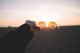 A pair of sunglasses pointing towards the bright setting sun releasing vitamin D.