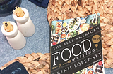 overhead photo of woven placemats, yellow candles in white holders, blue napkins and a book that reads “The Best American Food Writing” and “Kenji Lopez-Alt”