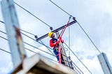 A line worker standing on a ladder does maintenance on a transmission line.