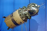 Color photograph of a model of the Vostok 1 spacecraft set against a blue background