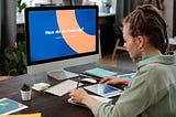An individual in front of the computer with the words “How do we keep up?” writing in a notebook and looking at a tablet with a chart on it