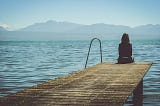 Woman sitting on the edge of a dock looking at the water