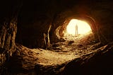 A human figure standing in front of a cave entrance.