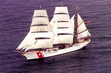 A large three-masted U.S. Coast Guard sailing ship is under full sail on the high seas.
