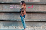 A woman beside a wall with “fear is the mind killer” written on it. Fear Is Always There, But You Can Choose How It Impacts You