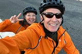 A man and a woman in orange jackets on a tandem bike