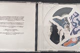 The open CD case with no CD. The background for both sides of the interior of the case is white. The left has the copyright information in centered black text. The right has a collage of fractured images in a circular shape where the CD would go.