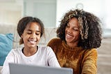 Smiling mother and young teen daughter doing homework at laptop