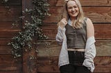 Madi Woll stands in front of an ivy covered wall constructed out of wood.