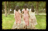 Three young women with their backs to us, walking side by side like friends or sisters