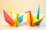 Two multicolored folded paper cranes facing each other.