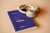 Notebook with “think” on it and headphones on a minimalist office desk.