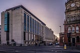 The University of Leeds School of Chemical Engineering Building at sunset, with pedestrians crossing the street next to The Library pub.