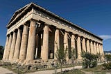 A well‑preserved ancient Greek temple with tall Doric columns stands in an open archaeological site, surrounded by small trees and a gravel path.