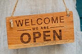 wood sign with written text on it: welcome — we are open.