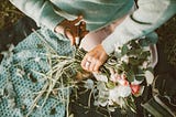 A cropped image of a woman in a soft turquoise sweater cutting flower stems in her lap.