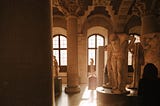 A woman, alone in a museum, looks at several statues.