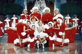Festive scene with entire cast gathered about Christmas tree and ballerina at the center.