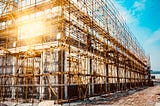 Image of a scaffolding under a bright blue sky, with sunlight shining through.