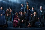 The cast of Fantastic Beasts 2 dressed as their characters in front of a blue dark background.