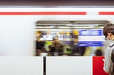 A man wearing a face mask looks at his phone while a train zooms by in the Tokyo subway.