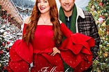 Falling for Christmas (2022) Movie Poster — Woman with hand on her hip, smiling in flamboyant red jumpsuit, man smiling and standing behind, off center of her