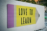 Sign with the image of a yellow pencil that has “love to learn” written on it.