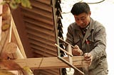 A man using a hand saw to cut a beam