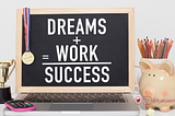 a chalkboard that says “Dreams+ Work = success” the chalkboard sits against a laptop and a gold medal is draped over it