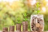 Three stacks and a jar of coins with small plants on each one.