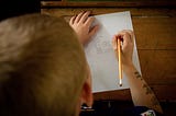 A kid writing words in his notebook using pencil