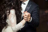 A cropped image of a bride and groom dancing, highlighting their closeness and hands clasped.