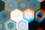 An abstract image of black and white hexagons. They are glitched, so there are colorful blips of red, blue and green coming off of them.