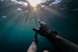 A drowning man reaches for the blue sky visible above the water