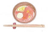 A bowl of reddish soup with a quartered lemon floating in it. A pair of wooden chopsticks are on a chopstick rest next to it.