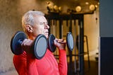 Older man doing resistance exercises with heavy dumbbells.