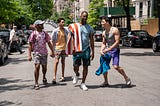 A scene from In The Heights featuring several characters standing on a road.