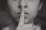 A woman places a finger to her lips, indicating ‘Ssshhh!’