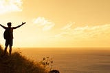 man with arms out on a hill overlooking the sea at sunset