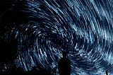 person standing in the dark with stars in a swirled galaxy overhead